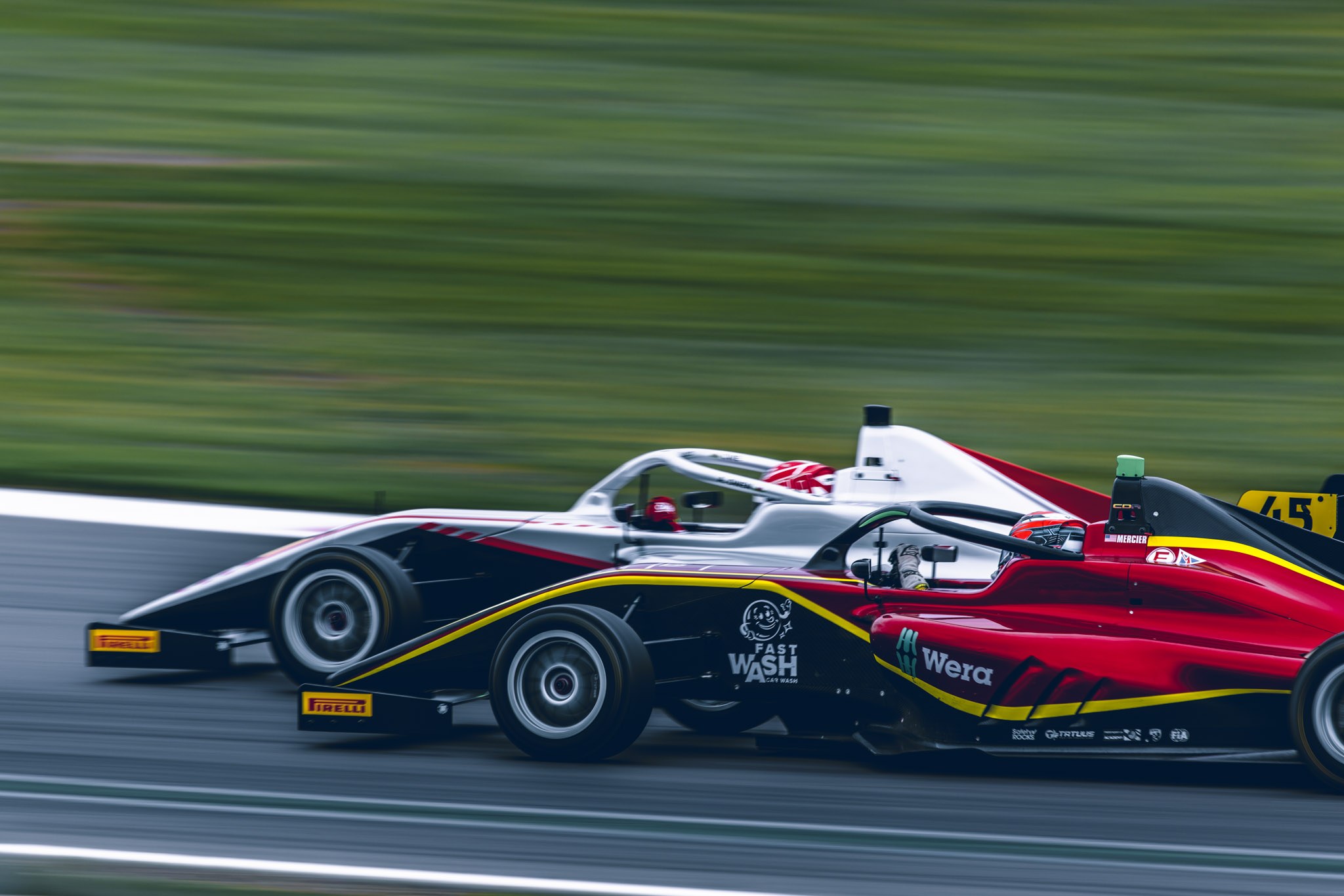 Two single-seater racing cars running side by side against a motion-blurred green background.